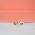 A rose gold ring with pavé-set clear stones, photographed on a white surface with a peach-pink background.