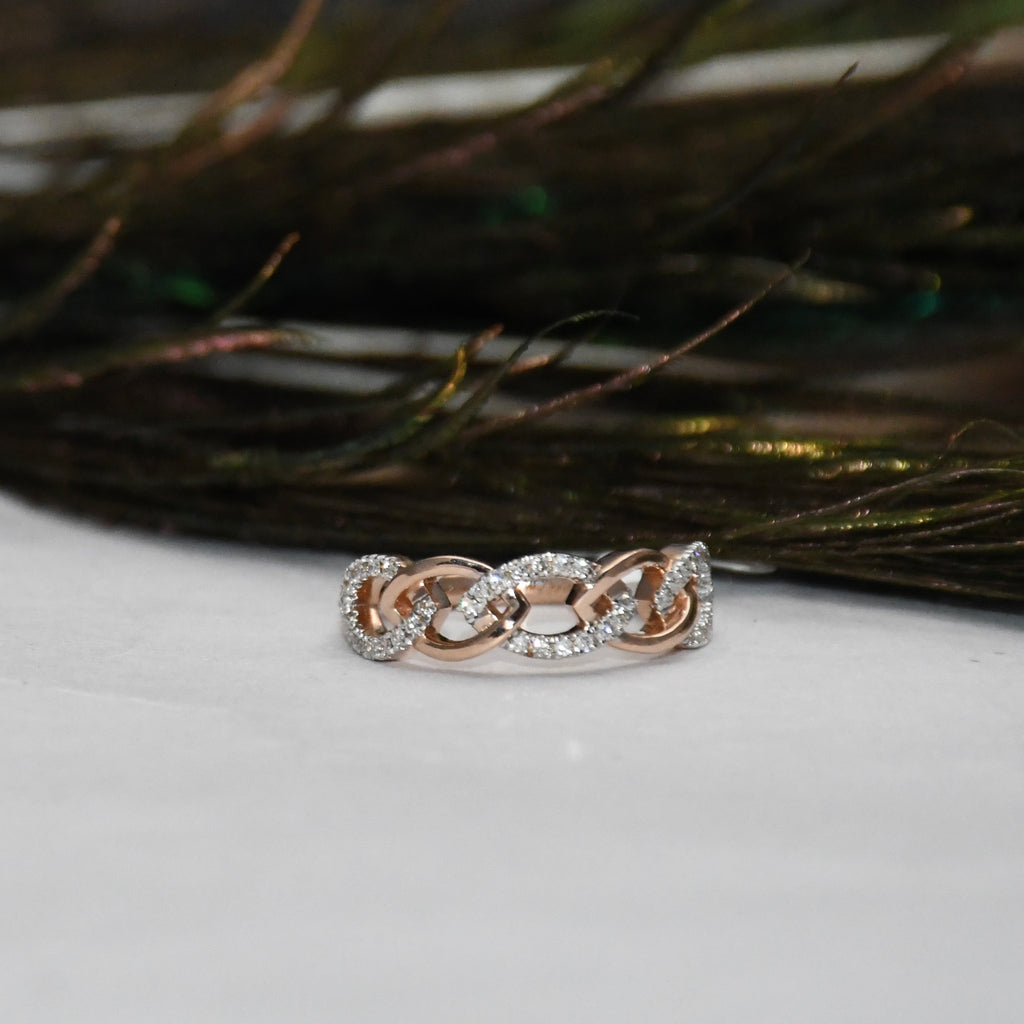 A delicate chain-link ring in rose gold, accented with small clear pavé stones, resting on a white surface with dark feathers in the background.