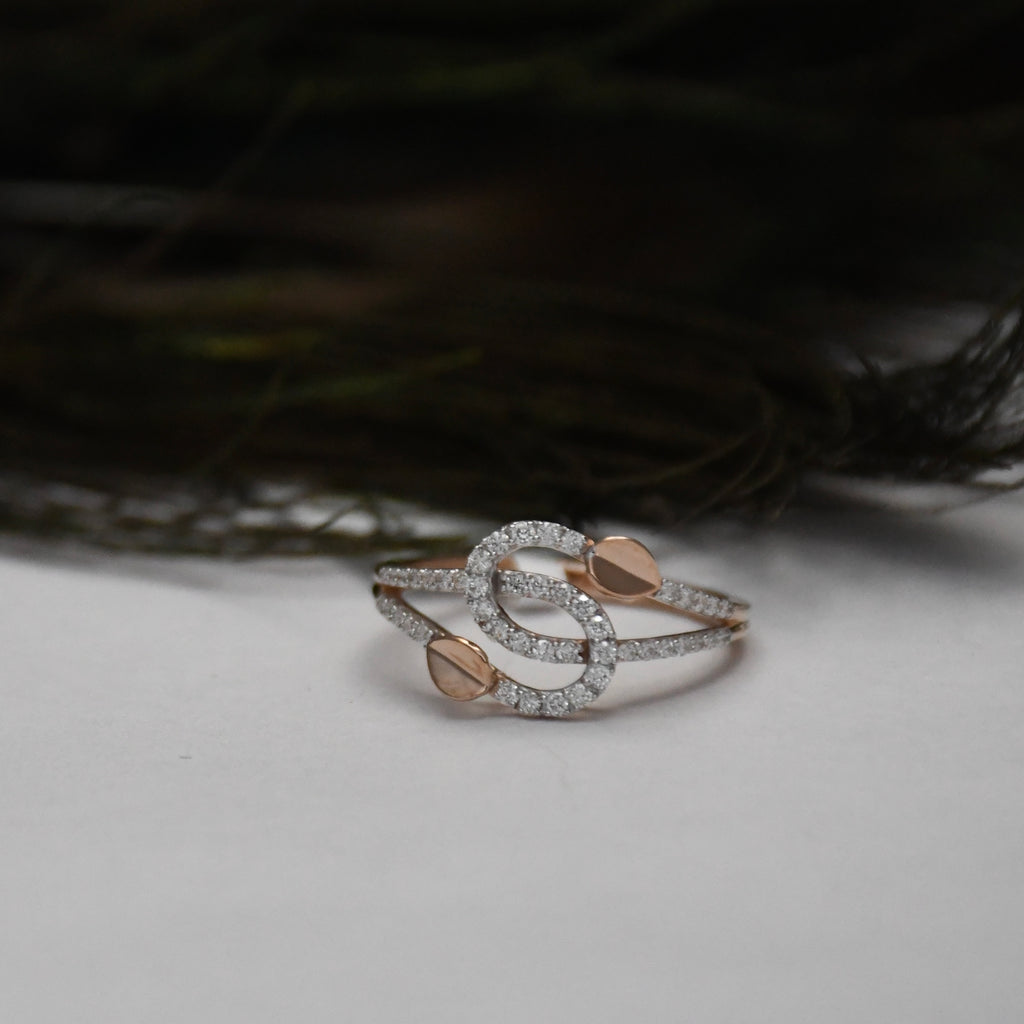A delicate ring with intertwined gold bands, accented by small pavé-set clear stones and two gold shaped details, resting on a light gray surface with a dark, blurred background.