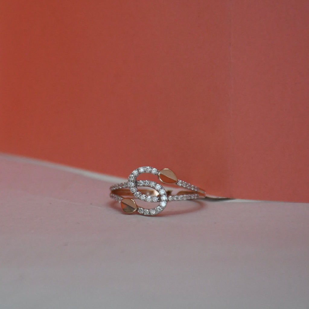 A delicate gold ring with pavé-set clear stones and two small unique shaped gold inlays, photographed on a two-toned surface with a warm coral background.