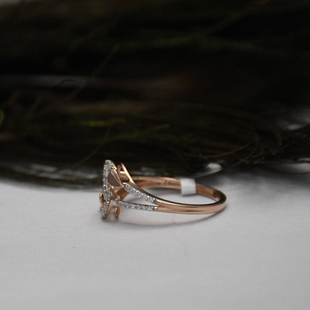 A rose gold ring with a triangular pavé diamond setting, resting on a light gray surface with a dark, blurred background.