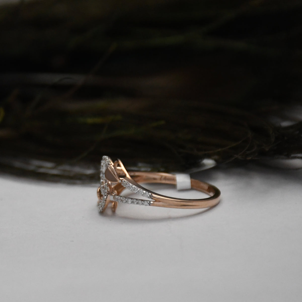 A rose gold ring with a triangular pavé diamond setting, resting on a light gray surface with a dark, blurred background.