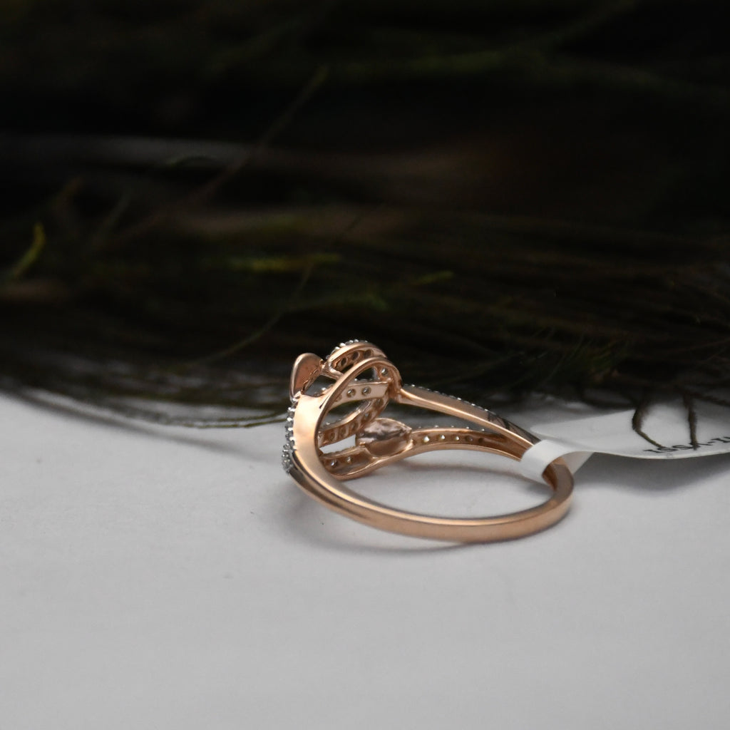 A rose gold ring with a complex, openwork filigree design and small clear stones, resting on a light gray surface with a dark, blurred background.
