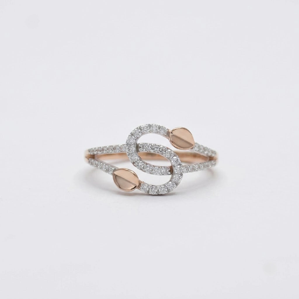 A delicate ring with intertwined gold bands, accented by small pavé-set clear stones and two gold leaf shaped details, resting on a white surface.