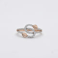 A delicate ring with intertwined gold bands, accented by small pavé-set clear stones and two gold leaf shaped details, resting on a white surface.