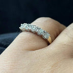 A close-up image of a white gold half eternity ring featuring a row of round brilliant-cut diamonds set in prongs, worn in a finger against a dark background, highlighting the sparkle and detailed craftsmanship of the ring.