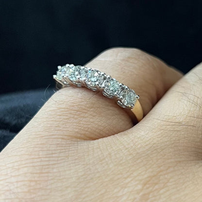A close-up image of a white gold half eternity ring featuring a row of round brilliant-cut diamonds set in prongs, worn in a finger against a dark background, highlighting the sparkle and detailed craftsmanship of the ring.