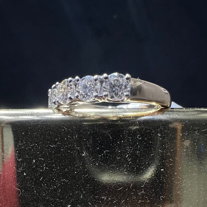 A close-up image of a white gold half eternity ring featuring a row of round brilliant-cut diamonds set in prongs, displayed on a reflective surface against a dark background, highlighting the sparkle and detailed craftsmanship of the ring.