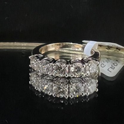 A close-up image of a white gold half eternity ring featuring a row of round brilliant-cut diamonds set in prongs, displayed on a reflective surface against a dark background, highlighting the sparkle and detailed craftsmanship of the ring.