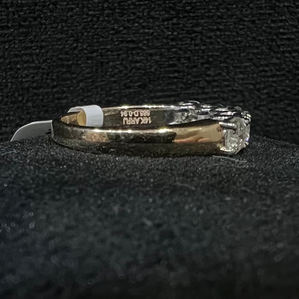 A close-up image of a white gold half eternity ring featuring a row of round brilliant-cut diamonds set in prongs, displayed on a rough surface against a dark background, highlighting the sparkle and detailed craftsmanship of the ring.