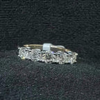 A close-up image of a white gold half eternity ring featuring a row of round brilliant-cut diamonds set in prongs, displayed on a rough surface against a dark background, highlighting the sparkle and detailed craftsmanship of the ring.
