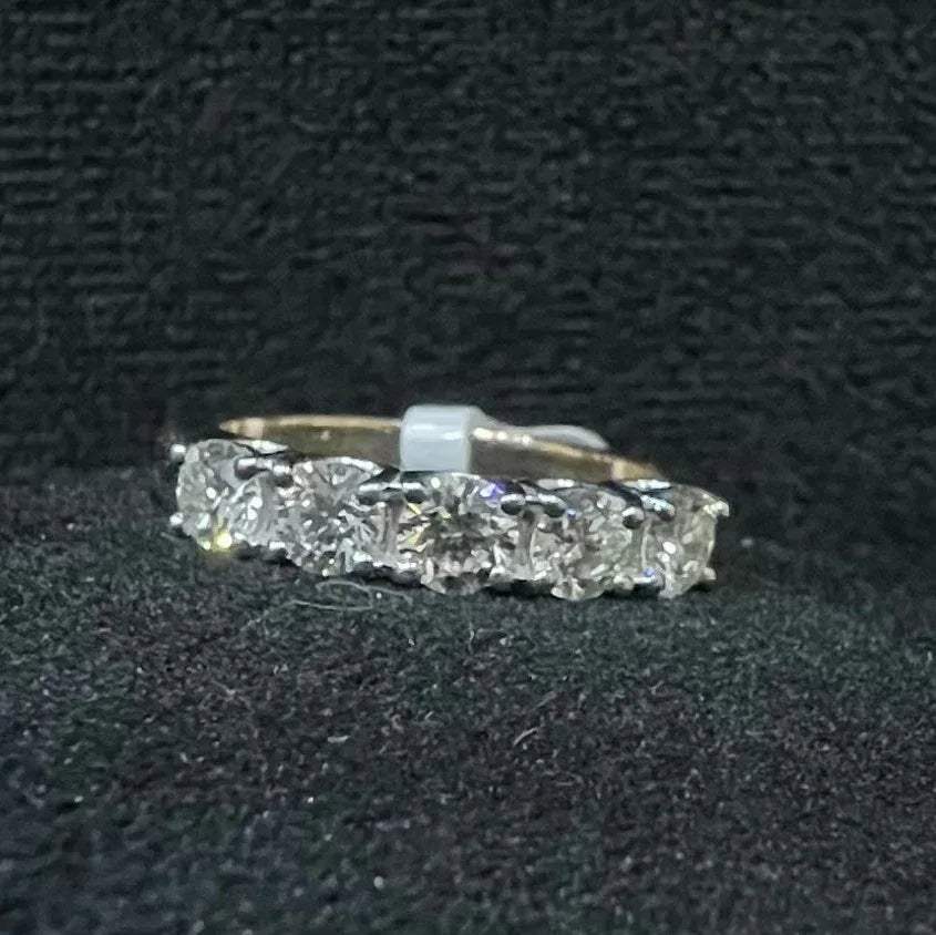 A close-up image of a white gold half eternity ring featuring a row of round brilliant-cut diamonds set in prongs, displayed on a rough surface against a dark background, highlighting the sparkle and detailed craftsmanship of the ring.