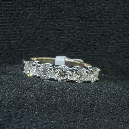 A close-up image of a white gold half eternity ring featuring a row of round brilliant-cut diamonds set in prongs, displayed on a rough surface against a dark background, highlighting the sparkle and detailed craftsmanship of the ring.