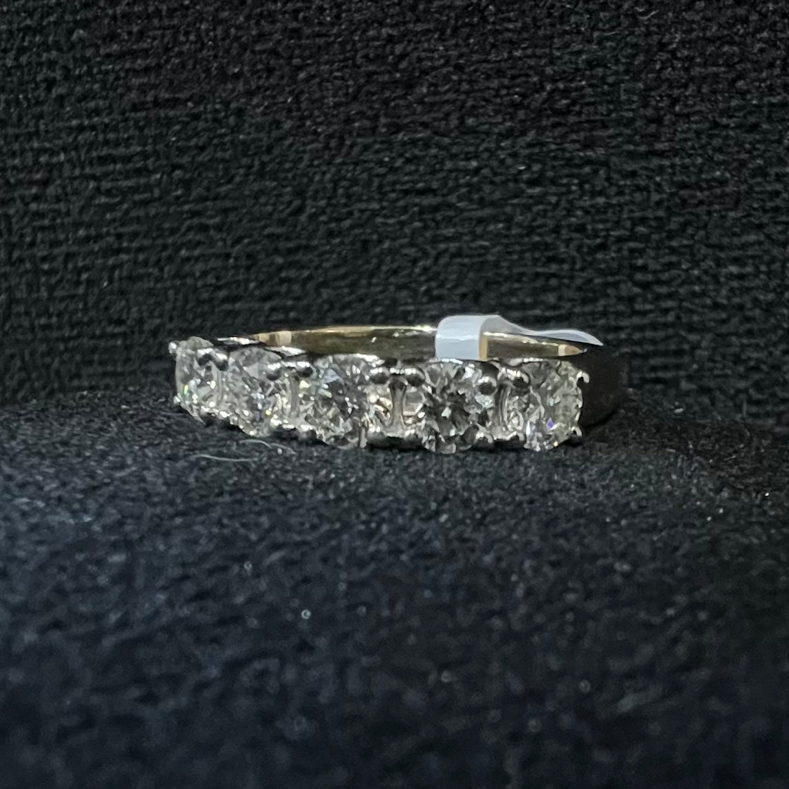 A close-up image of a white gold half eternity ring featuring a row of round brilliant-cut diamonds set in prongs, displayed on a rough surface against a dark background, highlighting the sparkle and detailed craftsmanship of the ring.