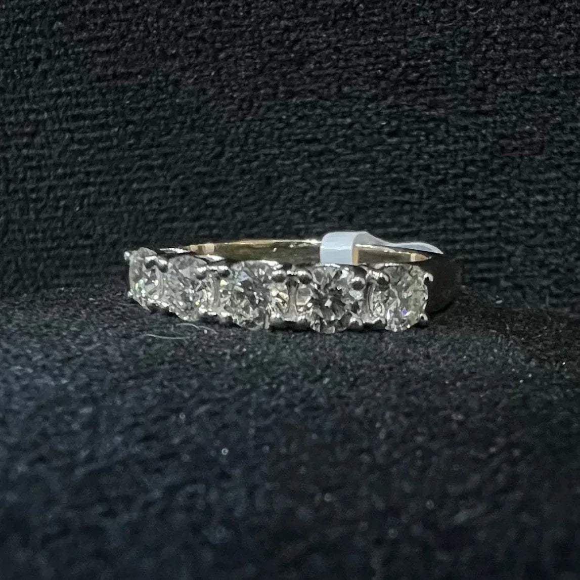 A close-up image of a white gold half eternity ring featuring a row of round brilliant-cut diamonds set in prongs, displayed on a rough surface against a dark background, highlighting the sparkle and detailed craftsmanship of the ring.