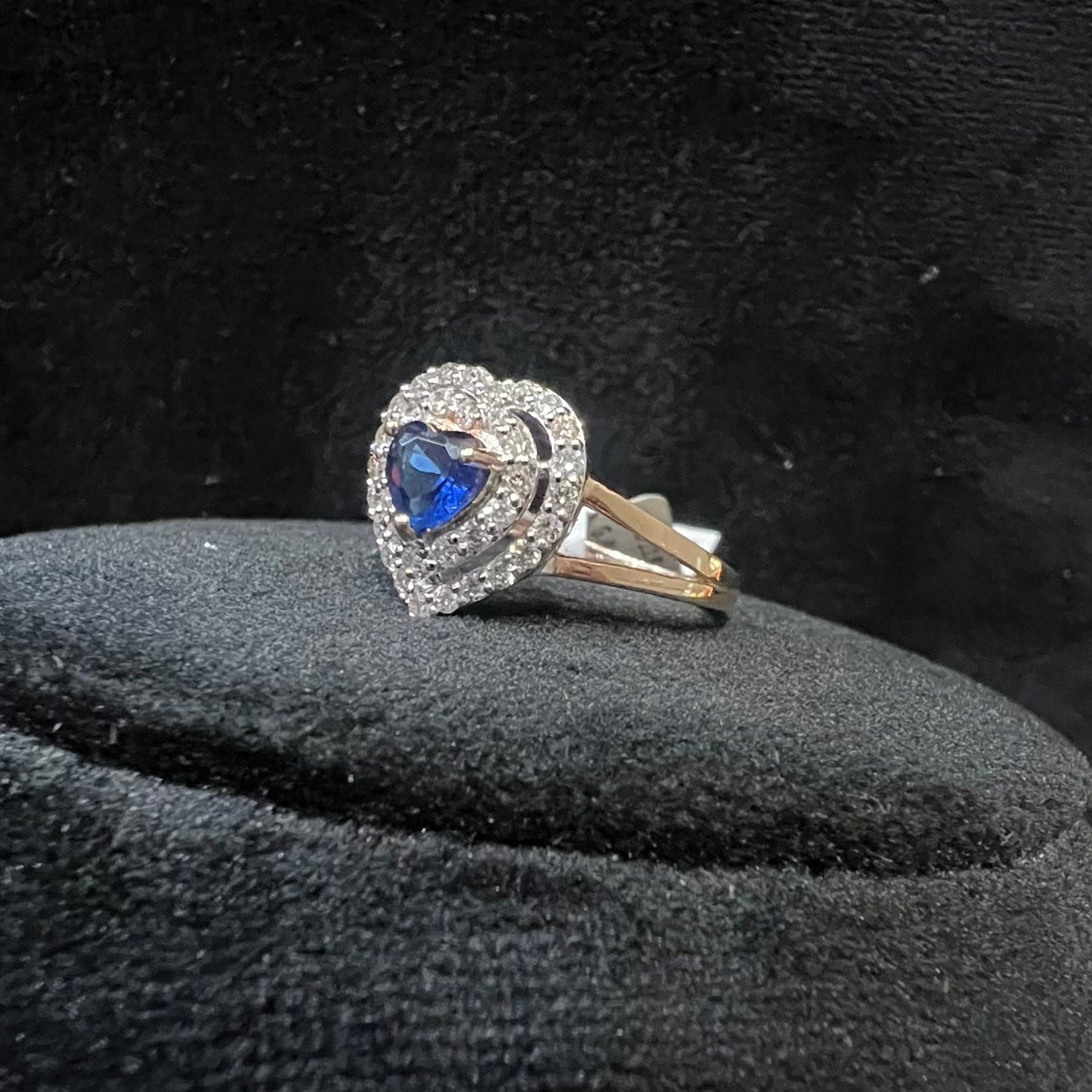 A gold ring with a central blue semi-precious stone, surrounded by smaller white diamonds, displayed on a black rough surface.