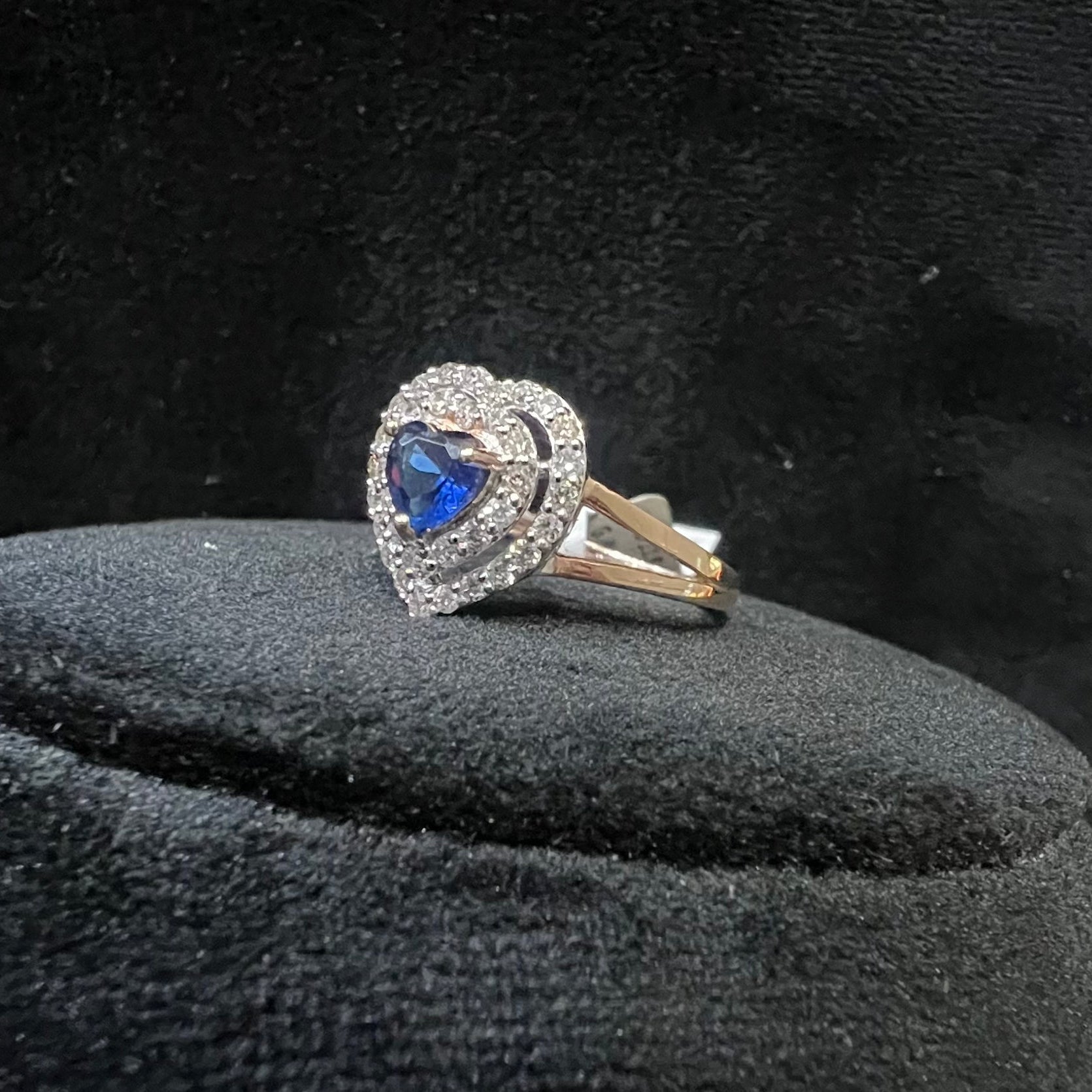 A gold ring with a central blue semi-precious stone, surrounded by smaller white diamonds, displayed on a black rough surface.