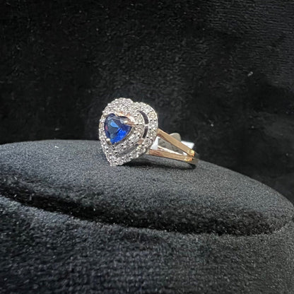 A gold ring with a central blue semi-precious stone, surrounded by smaller white diamonds, displayed on a black rough surface.