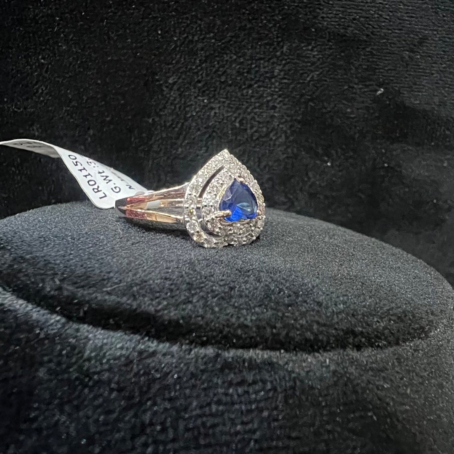 A gold ring with a central blue semi-precious stone, surrounded by smaller white diamonds, displayed on a black rough surface.