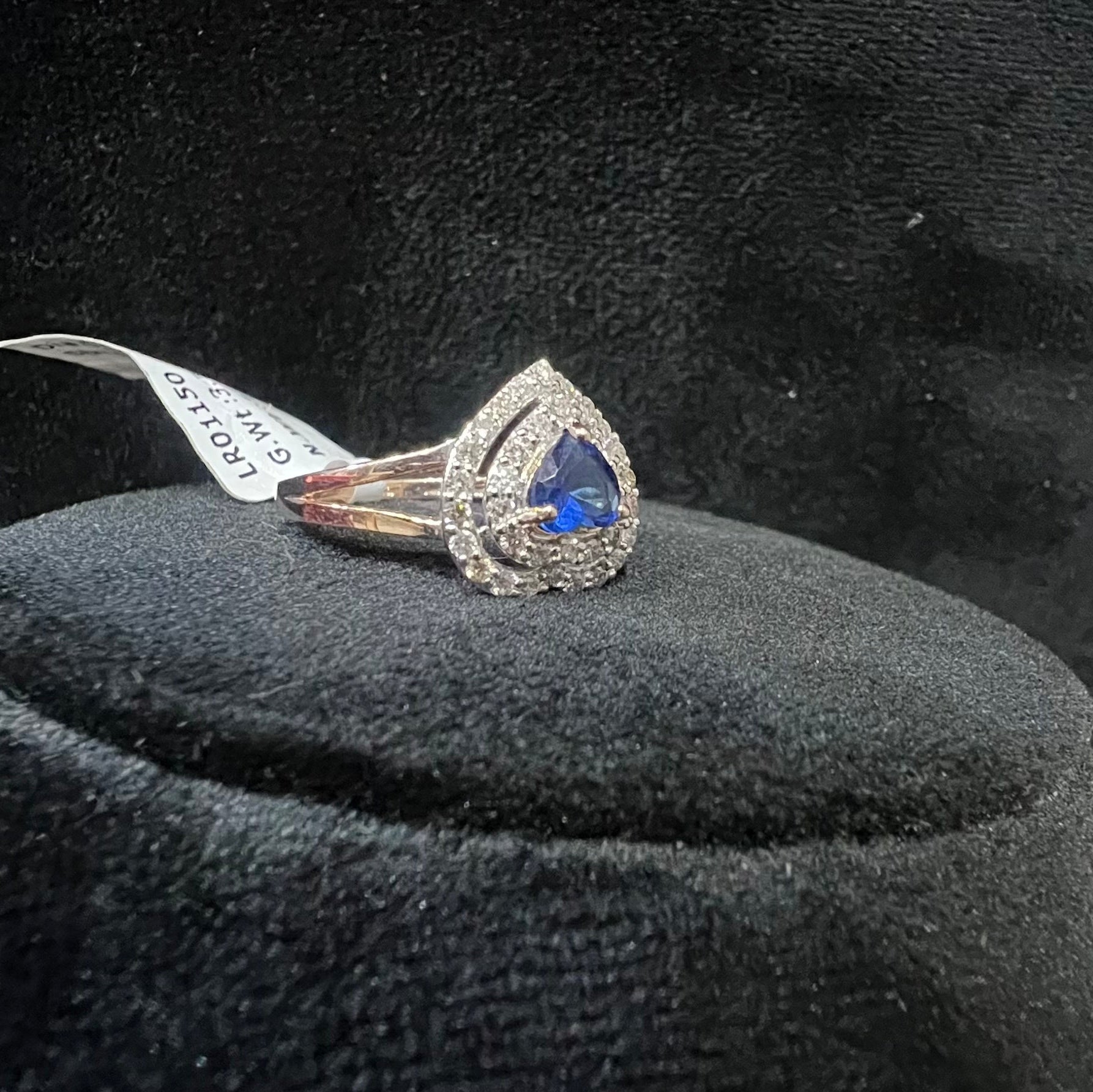 A gold ring with a central blue semi-precious stone, surrounded by smaller white diamonds, displayed on a black rough surface.
