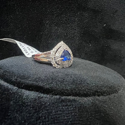 A gold ring with a central blue semi-precious stone, surrounded by smaller white diamonds, displayed on a black rough surface.