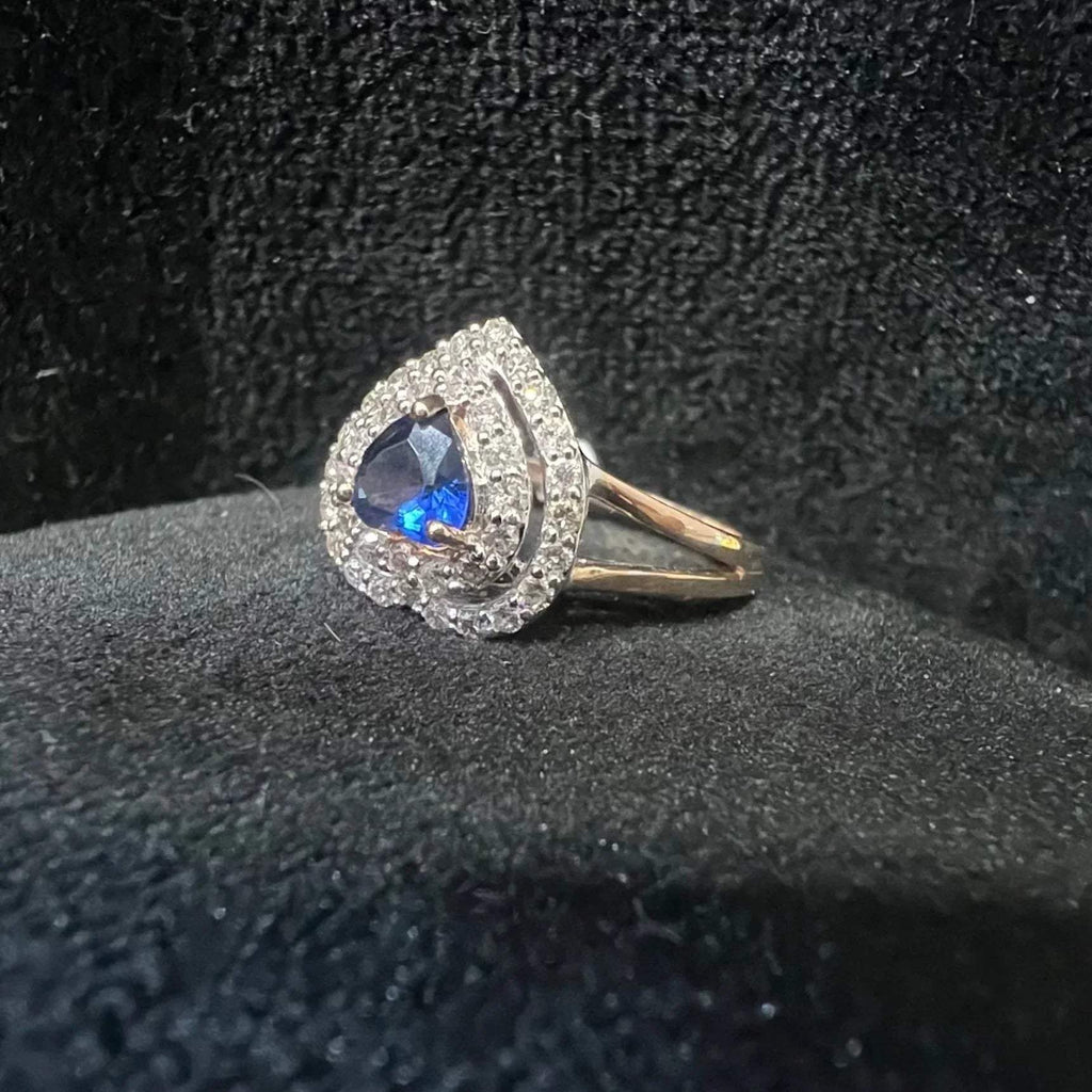 A gold ring with a central blue semi-precious stone, surrounded by smaller white diamonds, displayed on black rough surface.