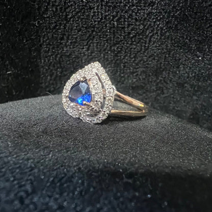 A gold ring with a central blue semi-precious stone, surrounded by smaller white diamonds, displayed on black rough surface.