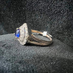 A gold ring with a central blue semi-precious stone, surrounded by smaller white diamonds, displayed on a black rough surface.