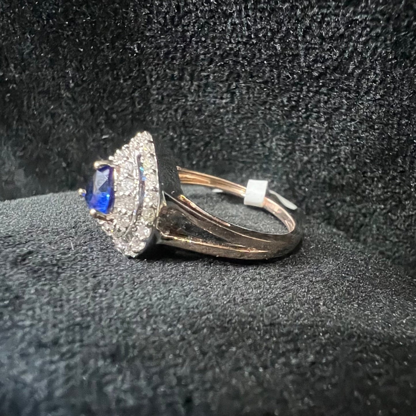 A gold ring with a central blue semi-precious stone, surrounded by smaller white diamonds, displayed on a black rough surface.