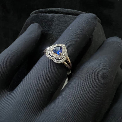 A gold ring with a central blue semi-precious stone, surrounded by smaller white diamonds, held in a gloved hand.