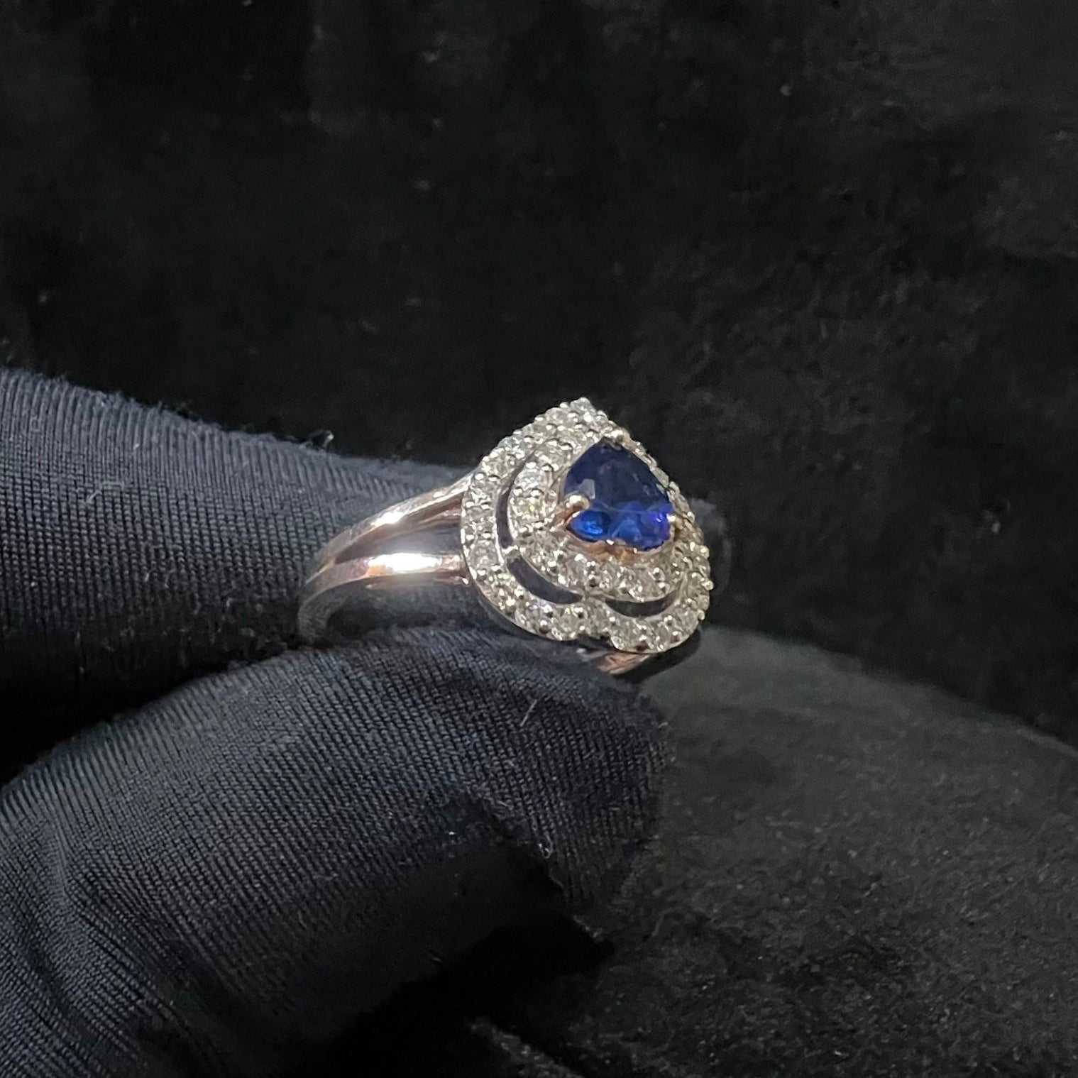 A gold ring with a central blue semi-precious stone, surrounded by smaller white diamonds, held in a gloved hand.