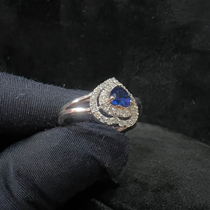 A gold ring with a central blue semi-precious stone, surrounded by smaller white diamonds, held in a gloved hand.