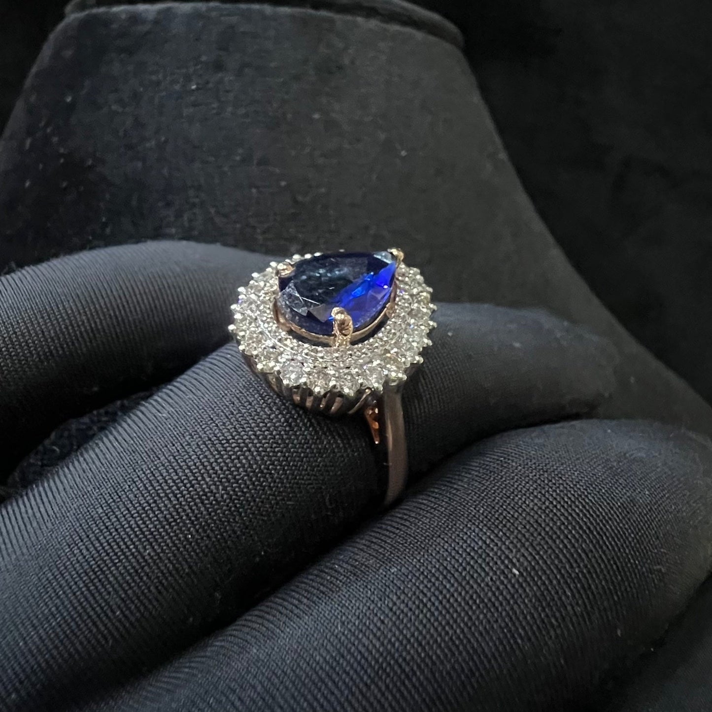 A gold band ring with a sparkling blue color stone and clear diamond set in a brilliant cut, displayed on a black mannequin hand.