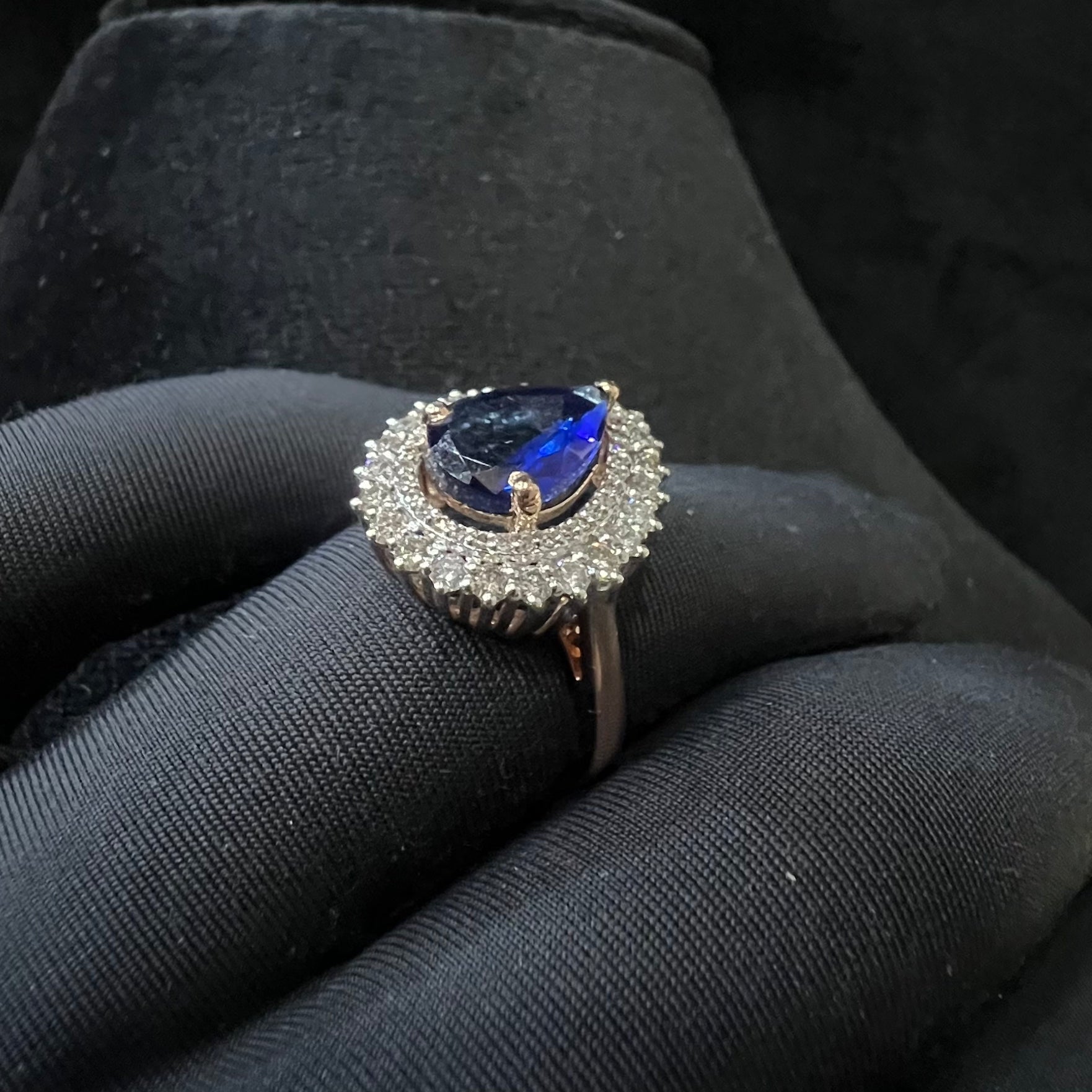 A gold band ring with a sparkling blue color stone and clear diamond set in a brilliant cut, displayed on a black mannequin hand.