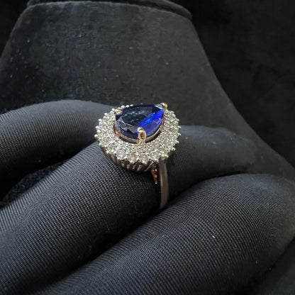 A gold band ring with a sparkling blue color stone and clear diamond set in a brilliant cut, displayed on a black mannequin hand.