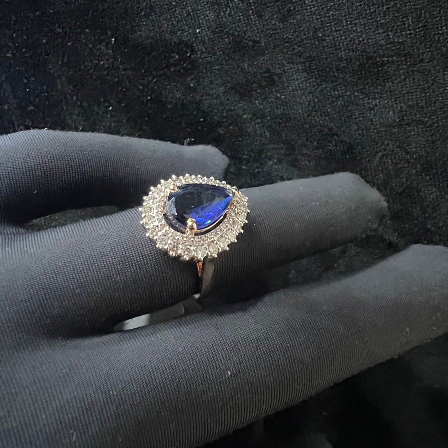 A gold band ring with a sparkling blue color stone and clear diamond set in a brilliant cut, displayed on a black mannequin hand.