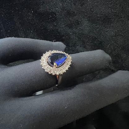 A gold band ring with a sparkling blue color stone and clear diamond set in a brilliant cut, displayed on a black mannequin hand.
