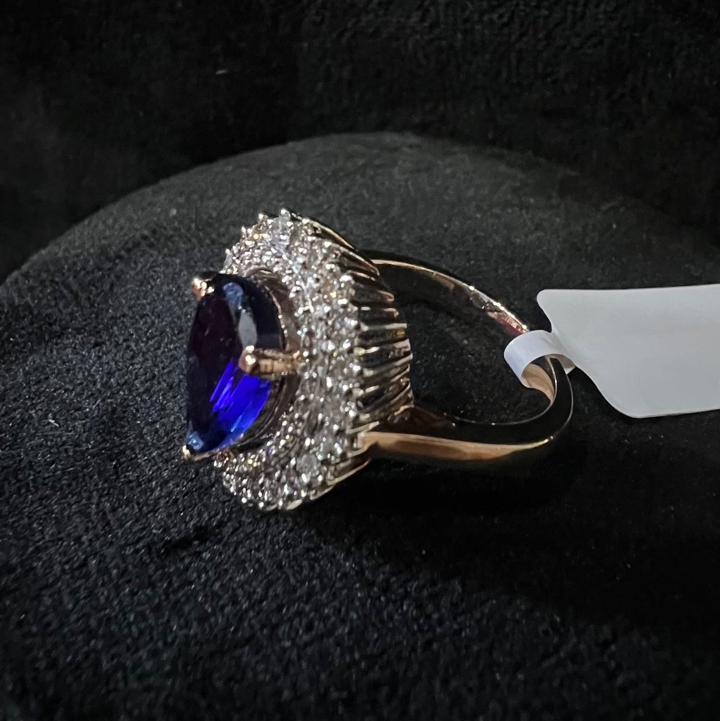 A gold band ring with a sparkling blue color stone and clear diamond set in a brilliant cut, displayed on a black mannequin bust.