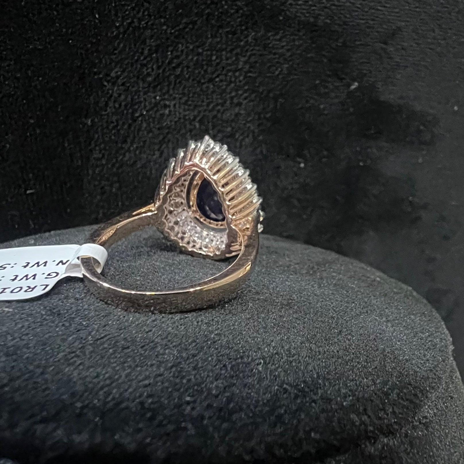 A gold band ring with a sparkling blue color stone and clear diamond set in a brilliant cut, displayed on a black mannequin bust.