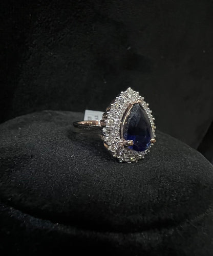 A gold band ring with a sparkling blue color stone and clear diamond set in a brilliant cut, displayed on a black mannequin bust.
