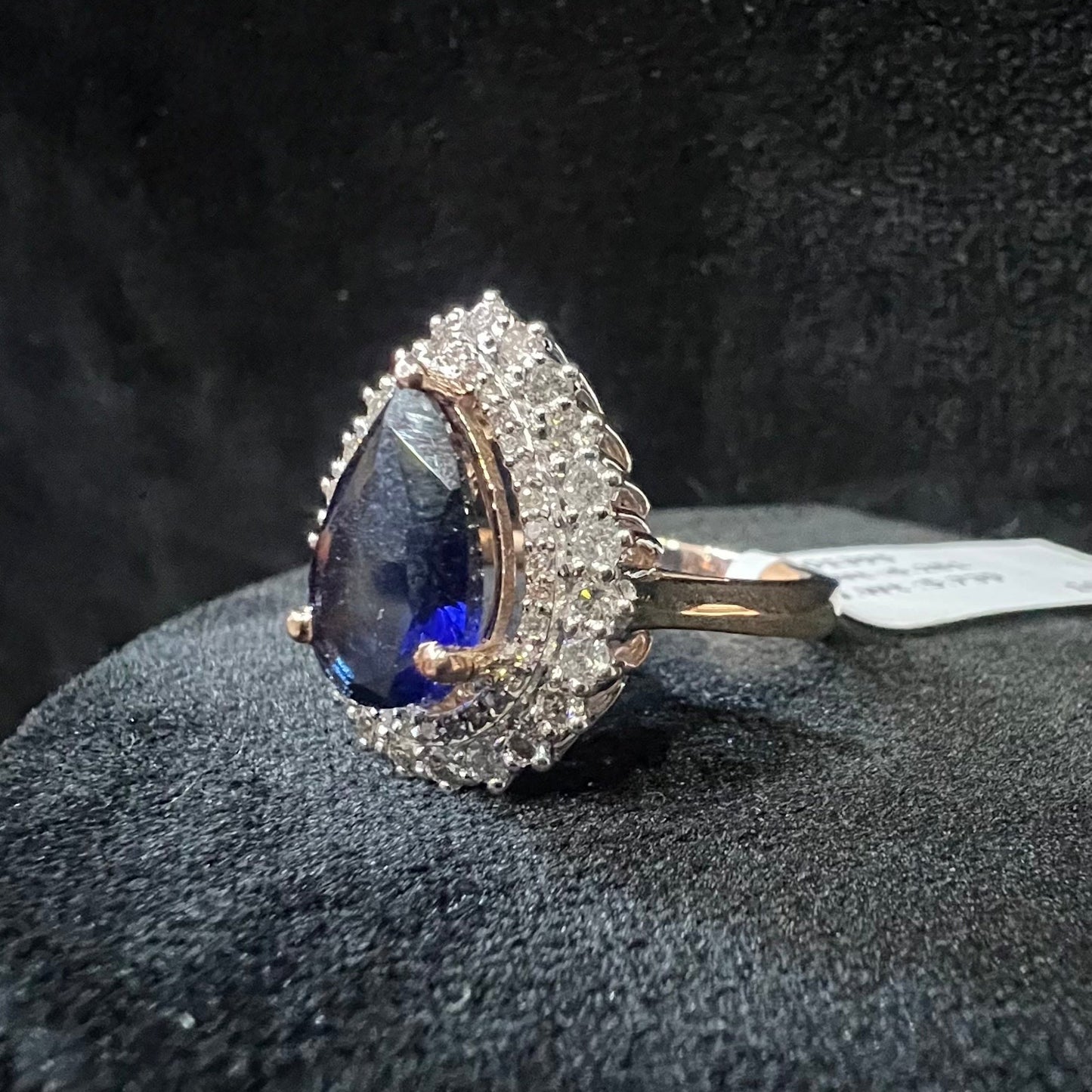 A gold band ring with a sparkling blue color stone and clear diamond set in a brilliant cut, displayed on a black mannequin bust.