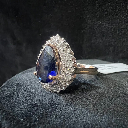 A gold band ring with a sparkling blue color stone and clear diamond set in a brilliant cut, displayed on a black mannequin bust.