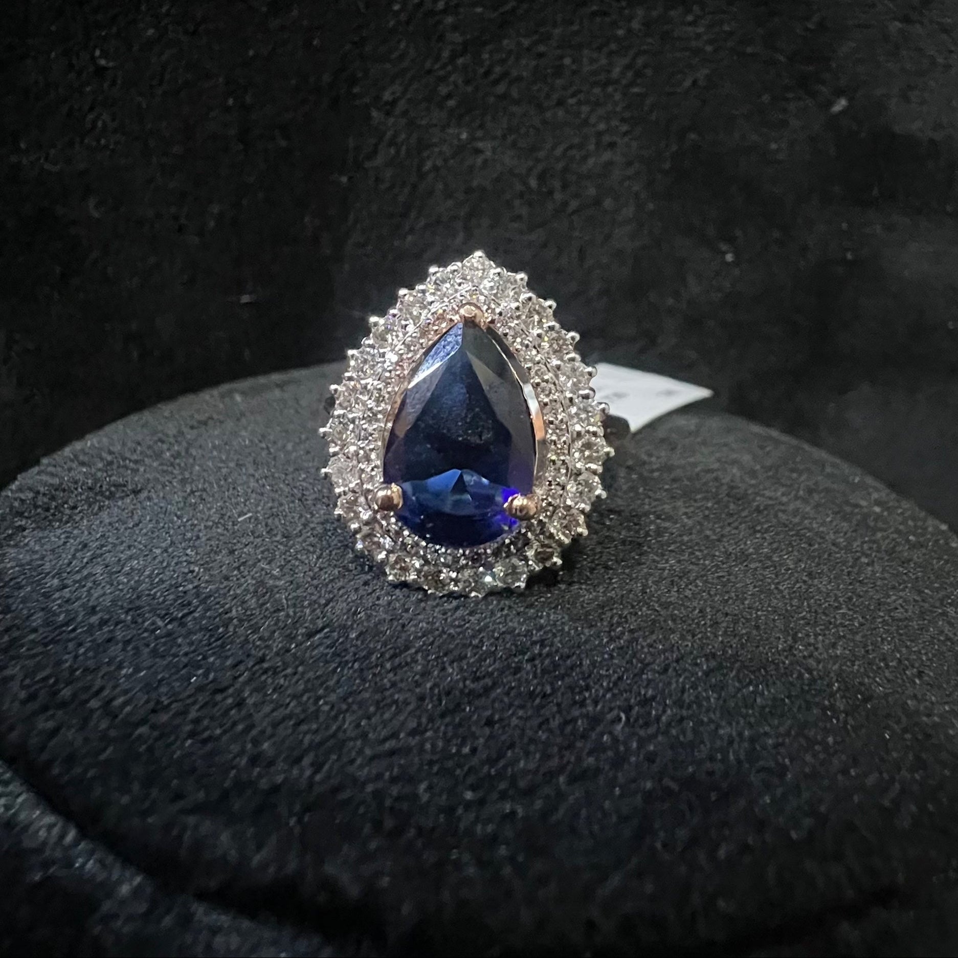 A gold band ring with a sparkling blue color stone and clear diamond set in a brilliant cut, displayed on a black mannequin bust.