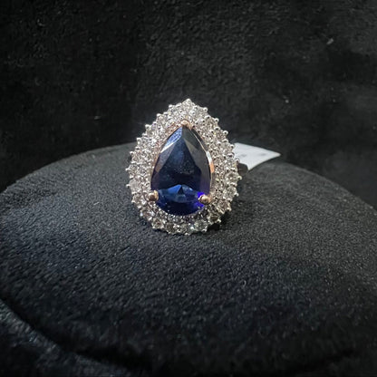 A gold band ring with a sparkling blue color stone and clear diamond set in a brilliant cut, displayed on a black mannequin bust.