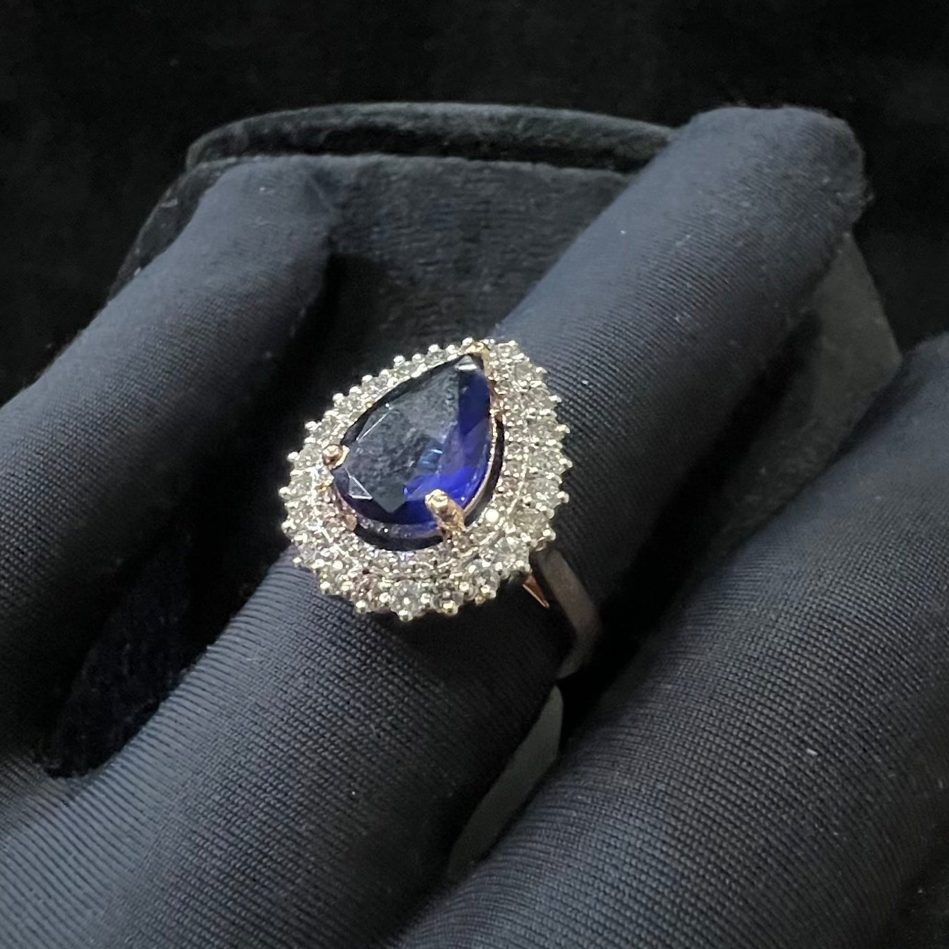 A gold band ring with a sparkling blue color stone and clear diamond set in a brilliant cut, displayed on a black mannequin hand.