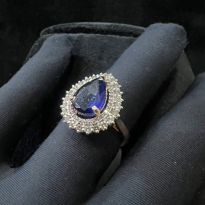 A gold band ring with a sparkling blue color stone and clear diamond set in a brilliant cut, displayed on a black mannequin hand.