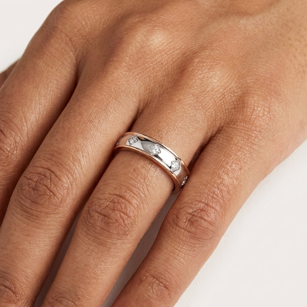 A close-up of band style diamond ring with the band split into two colors, white and rose gold, with diamonds set on the white gold section worn in a hand's finger.
