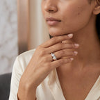 A gold diamond ring with a combination of white and rose gold, featuring a solitaire diamond on the top center and side diamonds along the band is worn in a woman's finger.