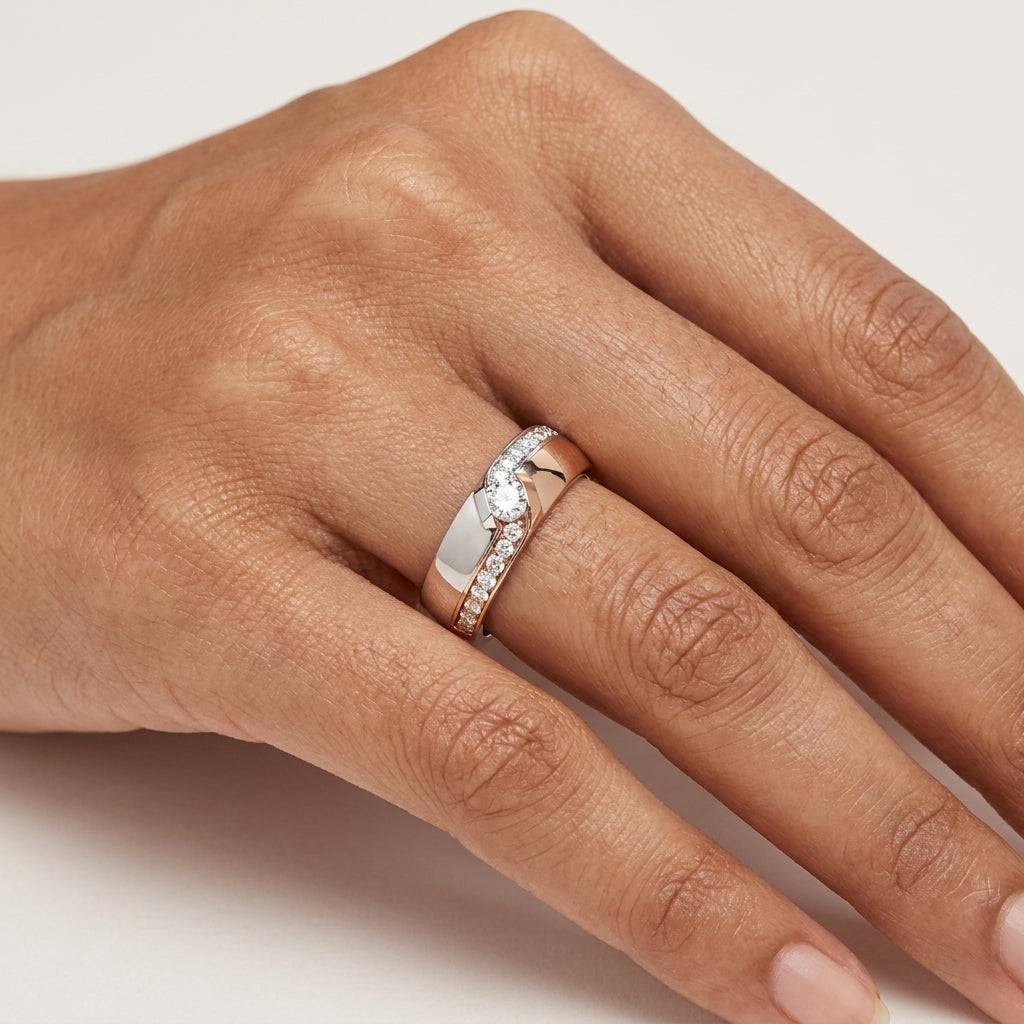 A gold diamond ring with a combination of white and rose gold, featuring a solitaire diamond on the top center and side diamonds along the band worn in a hand's finger.