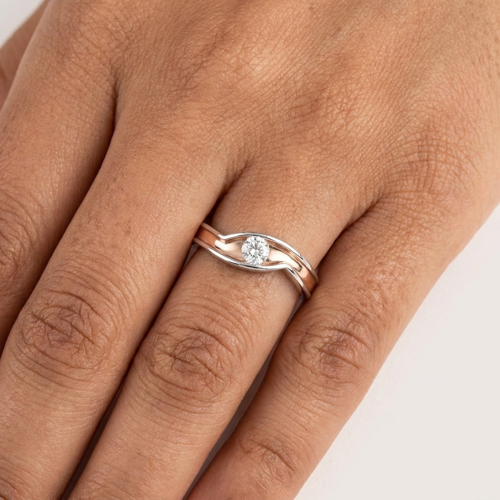 A solitaire diamond ring with a gold band featuring a single diamond at the center, set in a white gold or white gold band with a rose gold accent on the middle worn in a hand's finger against a white surface.